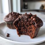 Close-up of a moist Chocolate Banana Muffins, cut in half showing the rich interior and chocolate chips on top.