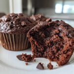 Close-up of a rich, dark Chocolate Banana Muffin with a bite taken out, showing the moist interior and chocolate chips.