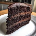 Close-up of a rich, moist slice of chocolate cake with thick chocolate frosting layers.