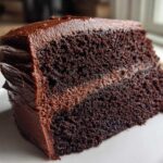 Close-up of a moist slice of dark chocolate cake with rich chocolate frosting and filling.