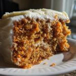 Close-up of a moist homemade carrot cake slice showing visible shredded carrots and thick cream cheese frosting.