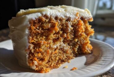Close-up of a moist homemade carrot cake slice showing visible shredded carrots and thick cream cheese frosting.