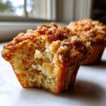 Close-up of a Pineapple Muffins With Crumb Topping, showing a bite taken out to reveal moist texture and pineapple chunks.
