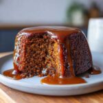 A close-up of a single serving of sticky toffee pudding recipe, drenched in rich toffee sauce.