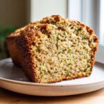Close-up of a freshly baked loaf of zucchini banana bread, showing the moist crumb and flecks of green zucchini.