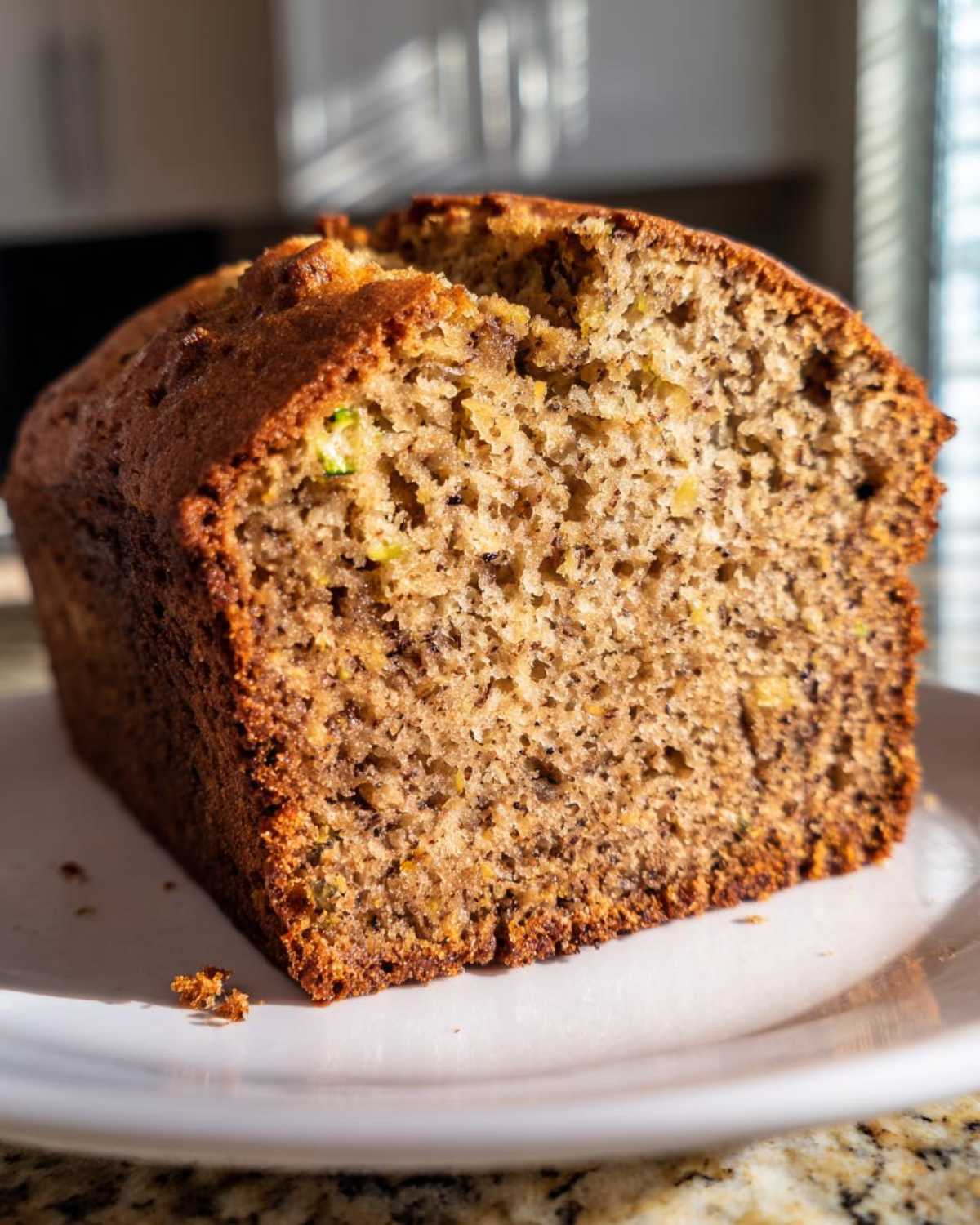 Close-up of a thick slice of moist zucchini banana bread showing its crumb texture and visible zucchini flecks.