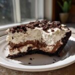 A close-up slice of no bake oreo pie showing chocolate and cream layers topped with cookie crumbles.