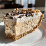 A close-up slice of no bake peanut butter pie on a white plate, topped with whipped cream, mini chocolate chips, and crumbs.