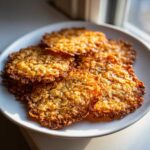 A stack of thin, golden brown oatmeal lace cookies glistening in the sunlight on a white plate.