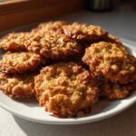 A pile of golden brown oatmeal lace cookies with crispy edges resting on a white plate, illuminated by sunlight.