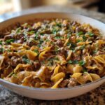 A close-up of creamy One Pan Ground Beef Stroganoff with egg noodles and ground beef, garnished with fresh parsley in a white skillet.