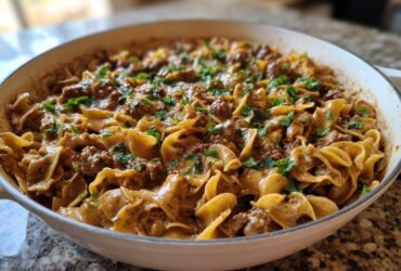 A close-up of creamy One Pan Ground Beef Stroganoff with egg noodles and ground beef, garnished with fresh parsley in a white skillet.