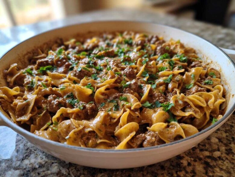 A close-up of creamy One Pan Ground Beef Stroganoff with egg noodles and ground beef, garnished with fresh parsley in a white skillet.