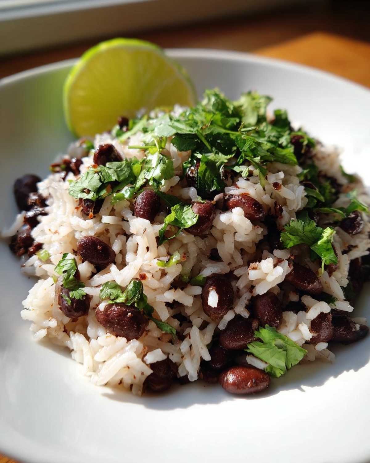 A close-up of a serving of white rice mixed with black beans and topped generously with fresh cilantro, with a lime wedge on the side.