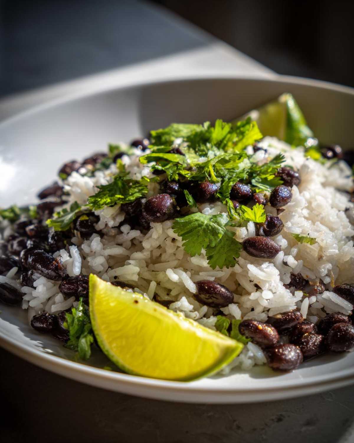 Close-up of fluffy white rice mixed with black beans, topped with fresh cilantro and a bright lime wedge, showcasing the beans and rice dish.