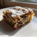 A single square of Ooey Gooey Banana Bars topped with powdered sugar, sitting on a white plate.