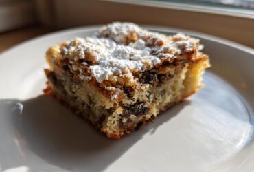 A single square of Ooey Gooey Banana Bars topped with powdered sugar, sitting on a white plate.