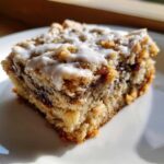 A square slice of ooey gooey banana bars topped with white icing, served on a white plate.