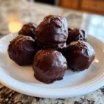 A pile of homemade Oreo Cake Balls coated in dark chocolate, resting on a white plate.