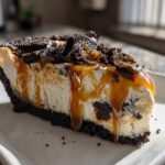 A decadent slice of ice cream pie featuring a dark cookie crust, creamy filling, and a thick caramel drizzle topped with cookie pieces.