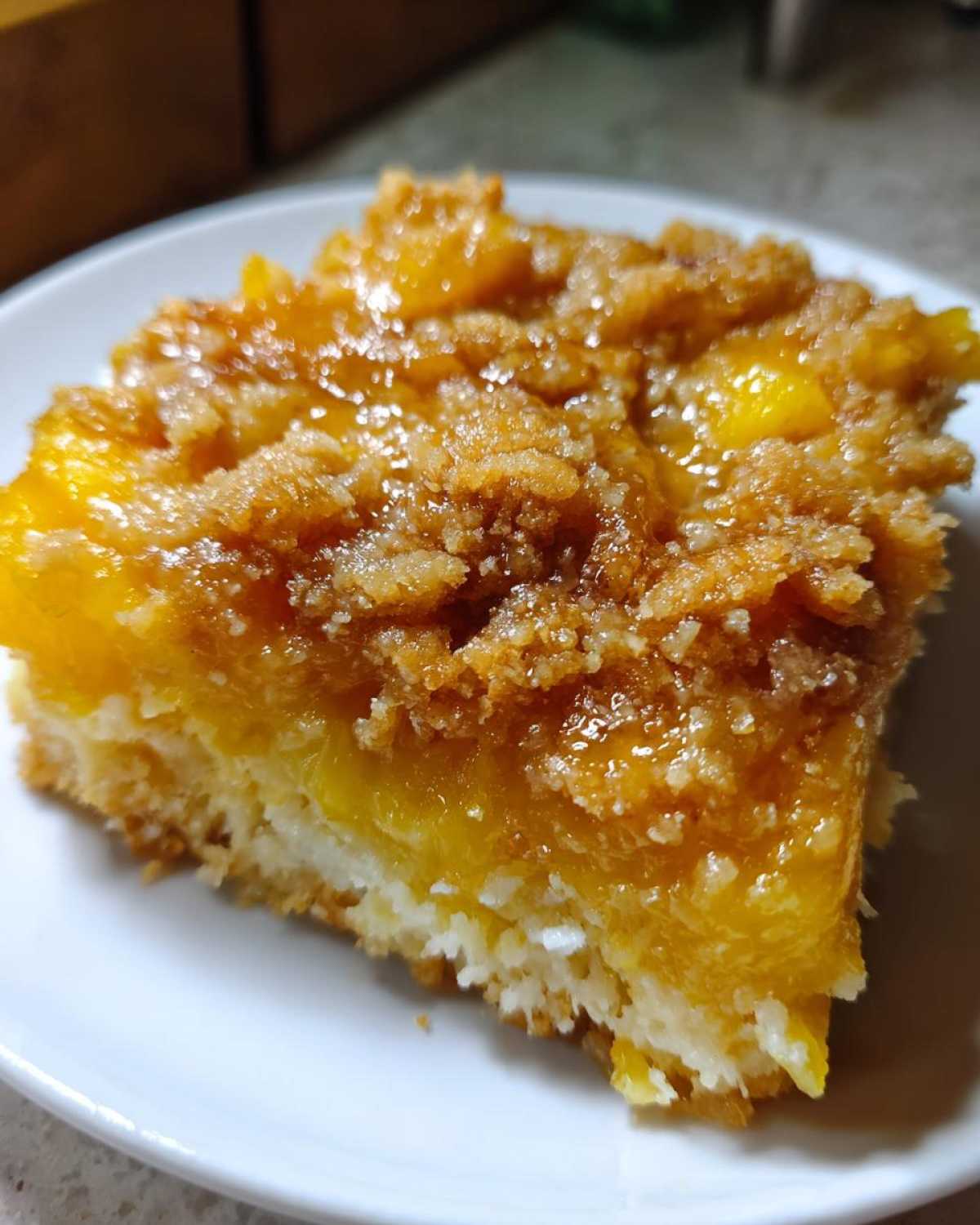 Close-up of a square slice of Paula Deen Pineapple Casserole showing a moist yellow pineapple layer and a sugary brown crumb topping.