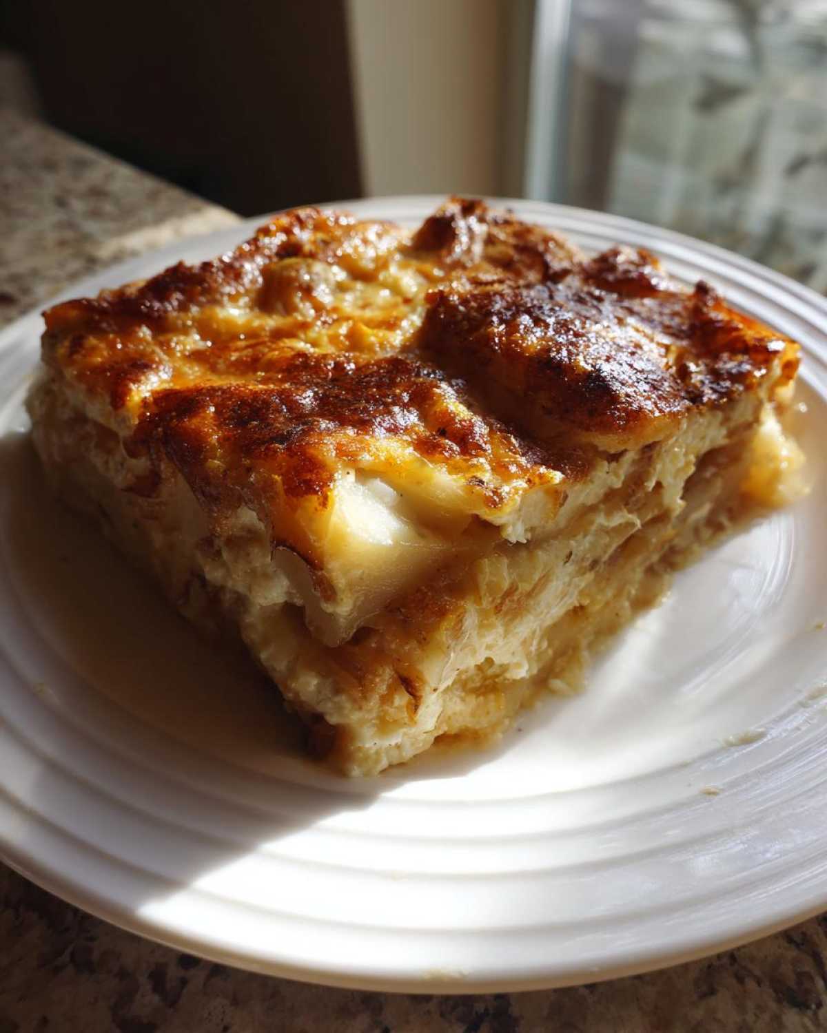 A square slice of creamy Paula Deen Scalloped Potatoes with a deeply browned, cheesy top, served on a white plate.
