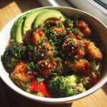 A close-up of Perfect Honey Mustard Chicken Bowls featuring glazed chicken pieces over quinoa with broccoli, avocado slices, and parsley.