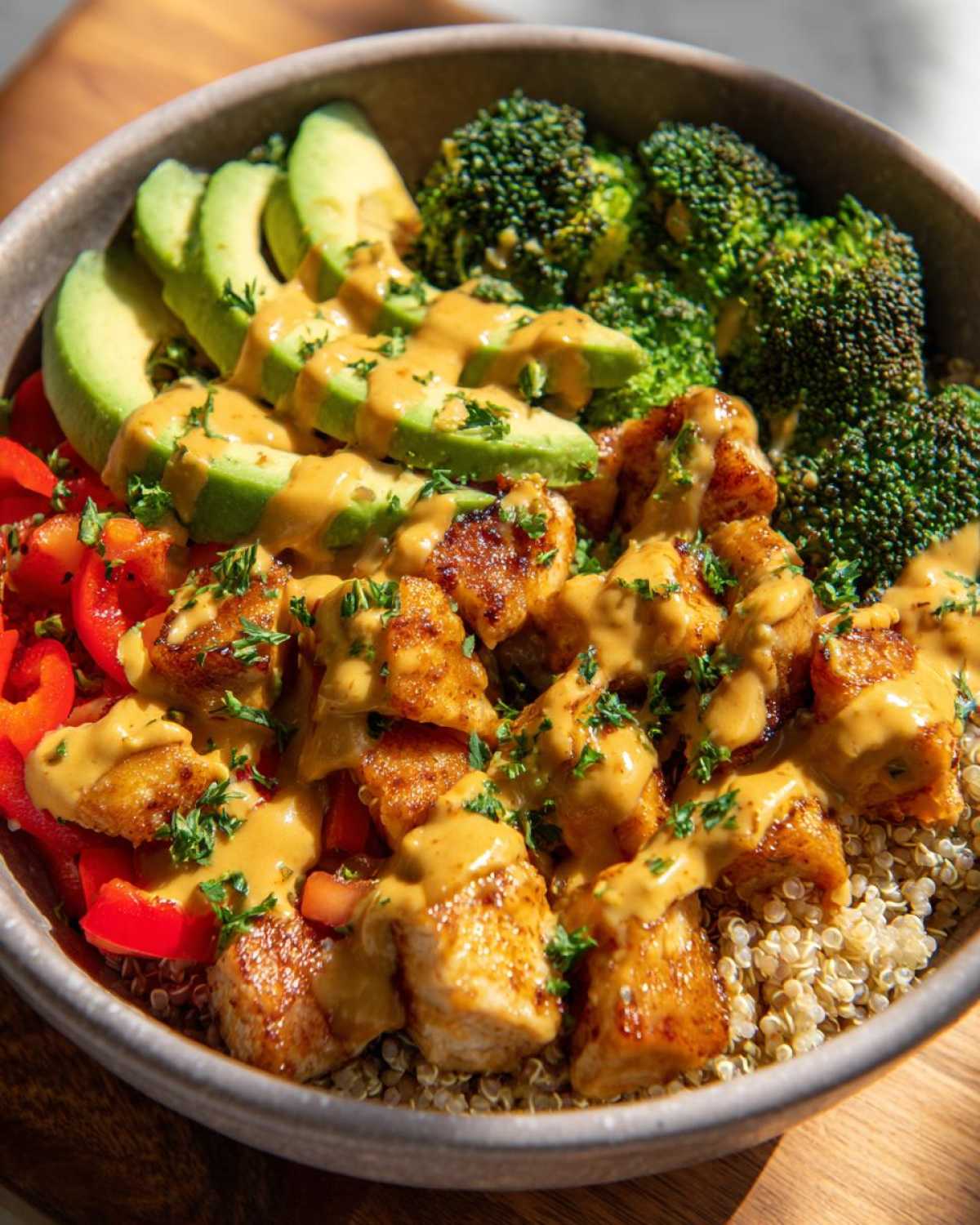 Close-up of a Perfect Honey Mustard Chicken Bowls featuring quinoa, seared chicken, avocado slices, broccoli, and red peppers drizzled with sauce.