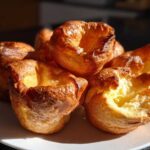 A close-up of several golden brown, perfectly risen yorkshire pudding on a white plate.
