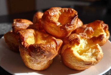 A close-up of several golden brown, perfectly risen yorkshire pudding on a white plate.
