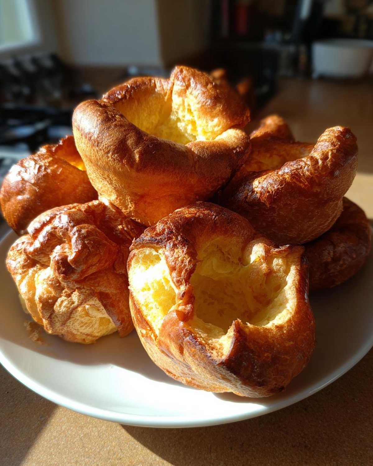 A close-up of several golden brown, perfectly risen Yorkshire pudding resting on a white plate.