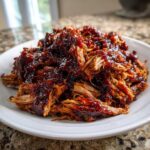 A close-up of shredded, saucy pioneer woman slow cooker pulled pork piled high on a white plate.