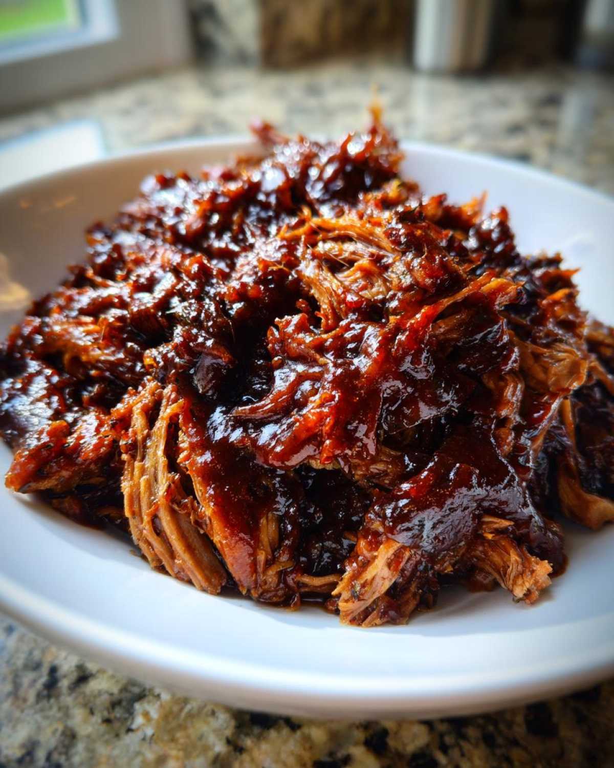 Close-up of shredded, saucy pioneer woman slow cooker pulled pork piled high in a white bowl.