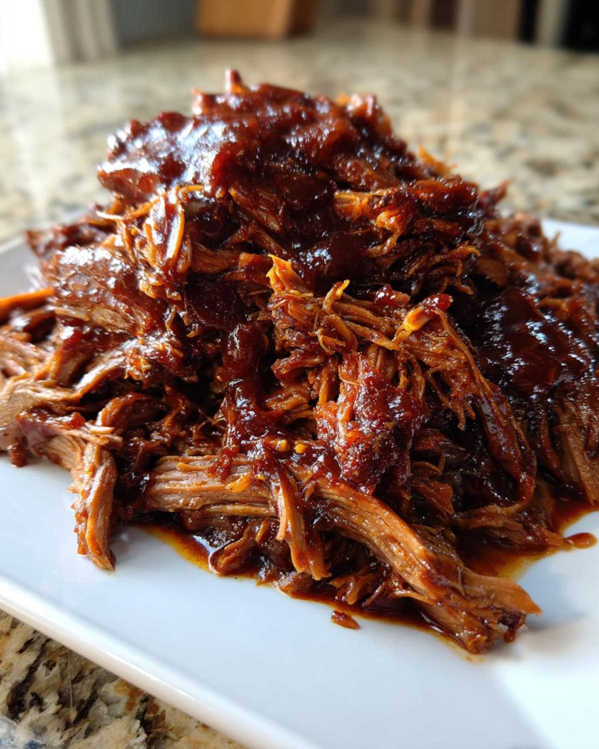 Close-up of tender, shredded pioneer woman slow cooker pulled pork smothered in rich barbecue sauce on a white plate.