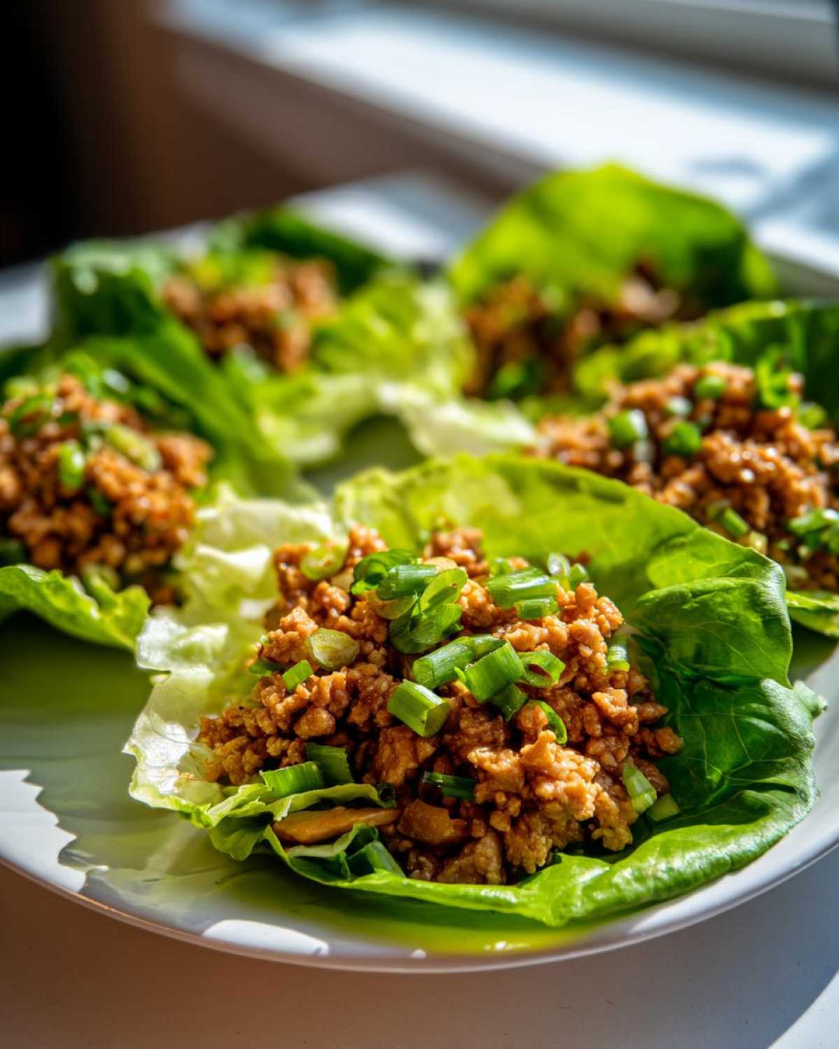 Close-up of several vibrant chicken lettuce wraps filled with savory ground chicken and topped with fresh green onions.