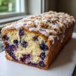 A loaf of Quick & Delicious Blueberry Streusel Coffee Cake with visible blueberries and a white glaze drizzle.