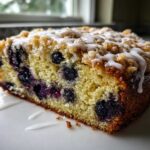 Close-up of a slice of Quick & Delicious Blueberry Streusel Coffee Cake with visible blueberries and white glaze.