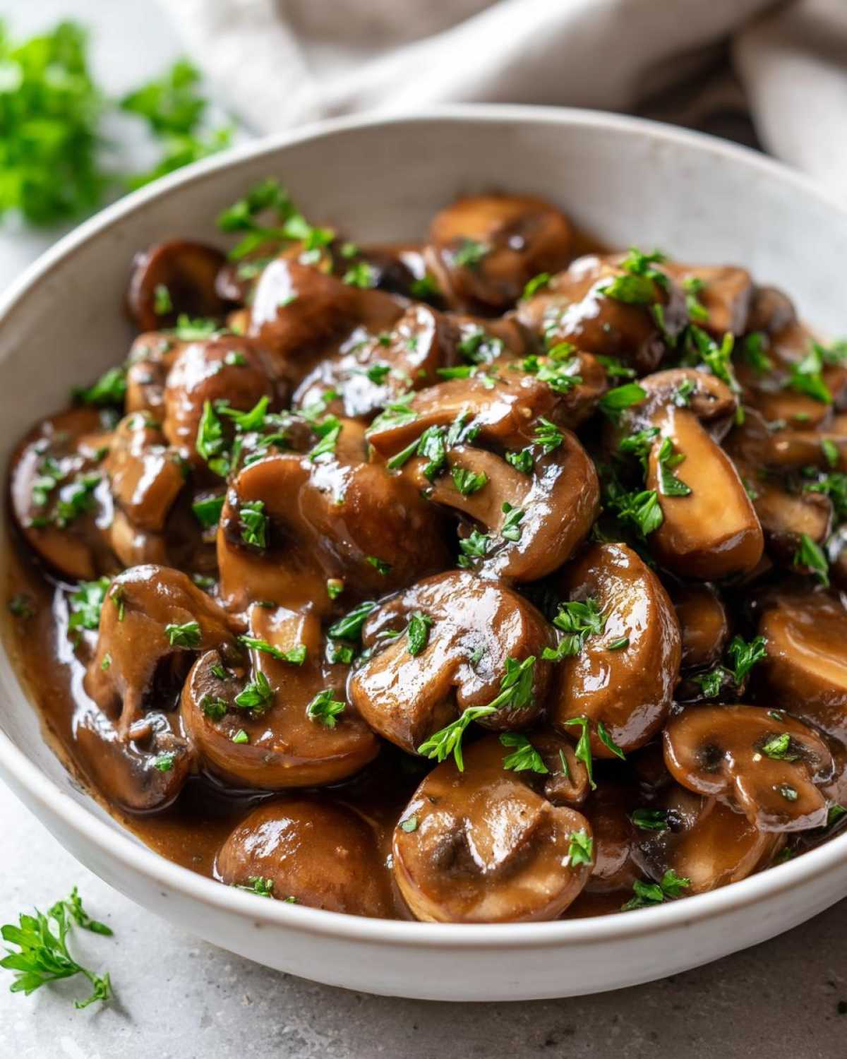 Close-up of whole button mushrooms coated in a rich, brown mushroom sauce and garnished with fresh parsley.