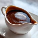 A close-up of rich, dark homemade brown gravy filling a small white ceramic gravy boat.