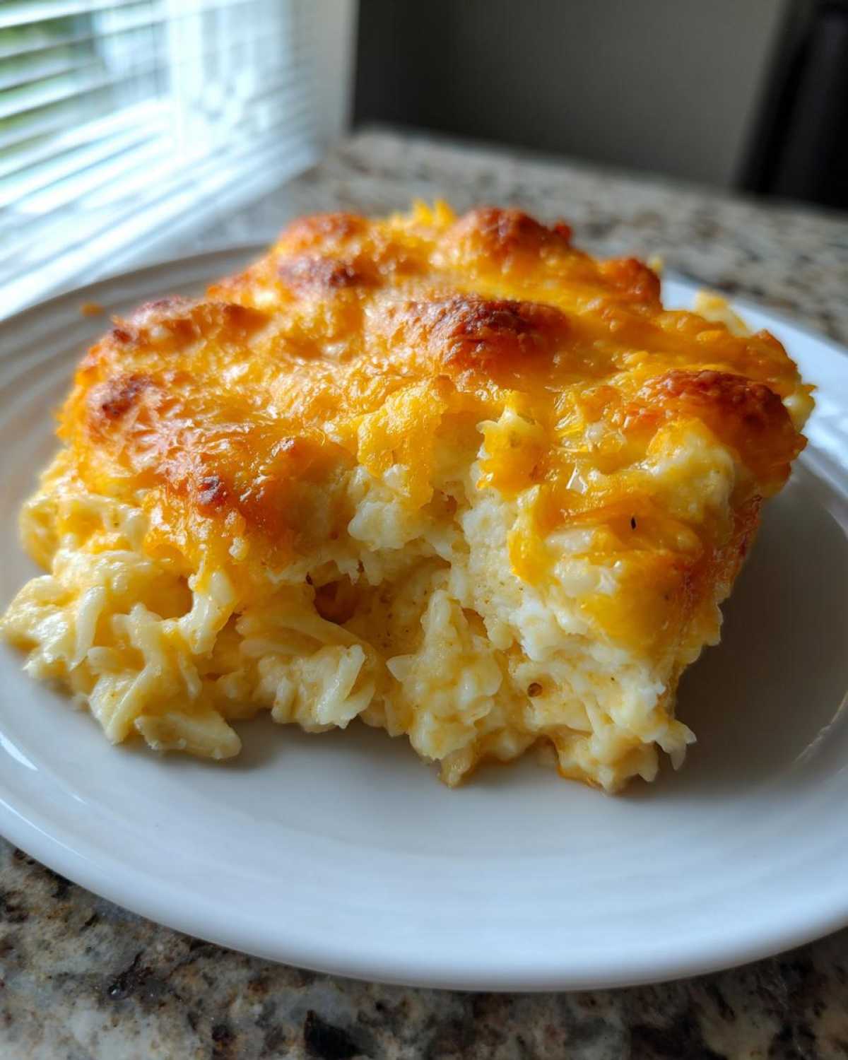 A close-up of a scoop of creamy funeral potatoes recipe topped with melted, browned cheddar cheese on a white plate.