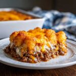 A close-up serving of tater tot casserole featuring crispy tater tots, ground beef, and melted cheddar cheese on a white plate.