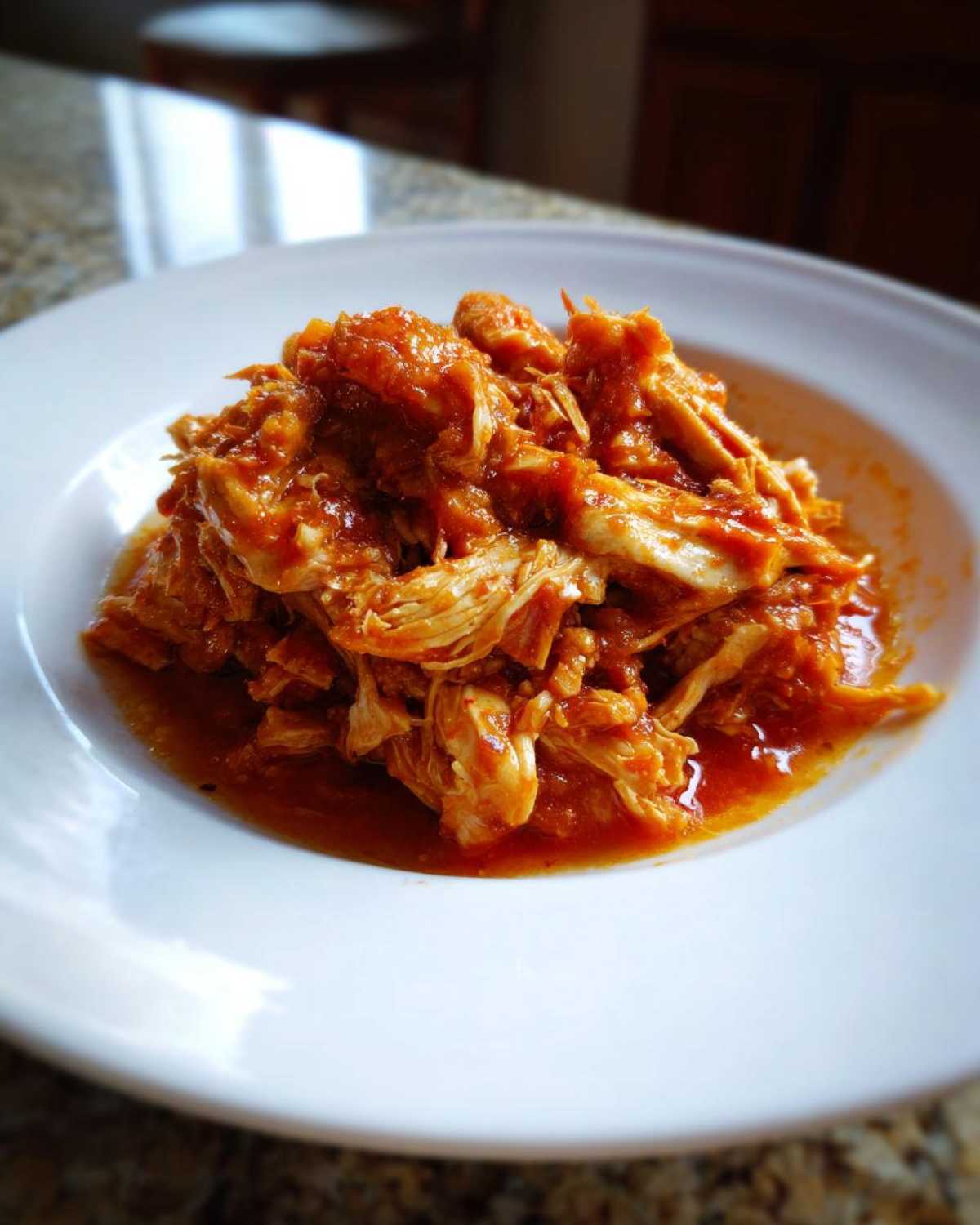 A close-up of shredded chicken tinga coated in a vibrant, savory red sauce served on a white plate.