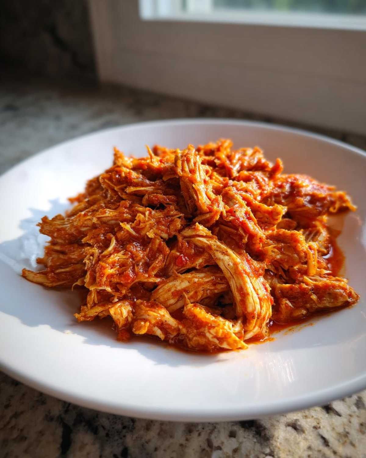 A close-up of richly sauced, shredded chicken tinga piled high on a white plate, ready to serve.