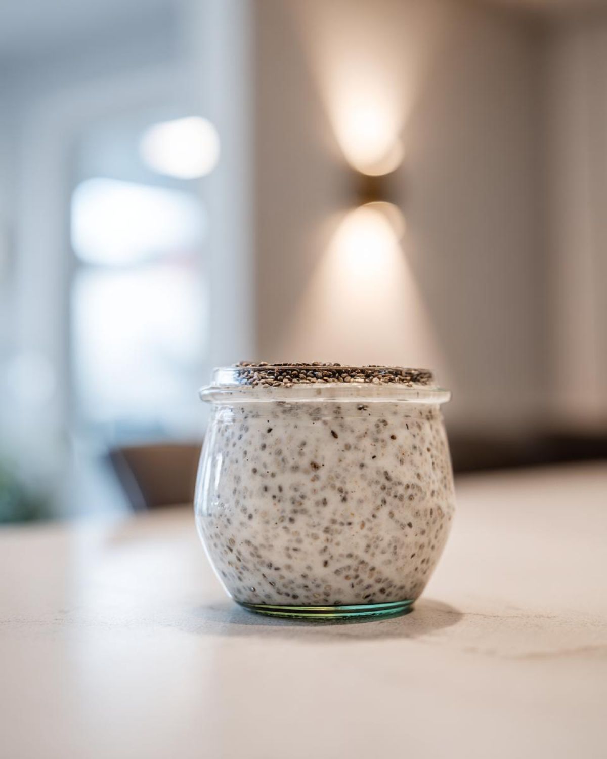 A glass jar filled with creamy chia seed pudding, topped with dry chia seeds, sitting on a light countertop.