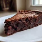 Close-up of a dense, fudgy slice of flourless chocolate cake with a slightly cracked top, served on a white plate.