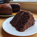A generous slice of moist german chocolate cake with thick chocolate frosting sits on a white plate.