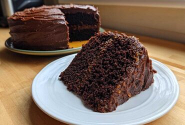 A generous slice of moist german chocolate cake with thick chocolate frosting sits on a white plate.