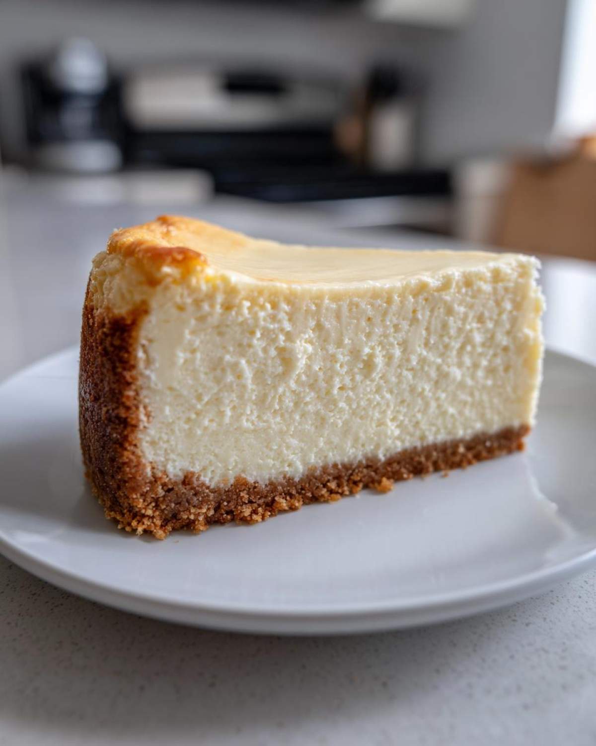 A thick, creamy slice of new york cheesecake with a golden-brown graham cracker crust, served on a white plate.