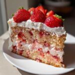 A perfect slice of strawberry cake layered with cream and fresh strawberries on top, ready to eat.
