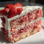 A moist, layered slice of strawberry cake with white frosting and topped with fresh sliced strawberries.